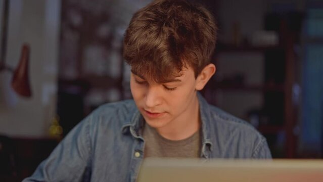 Teenage student learning at home with books and laptop computer. Online school and digital education, sitting at desk late night