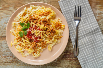 Pasta bolognese in tomato garnished with herbs and cheese in a plate on a wooden table next to a fork and a napkin.