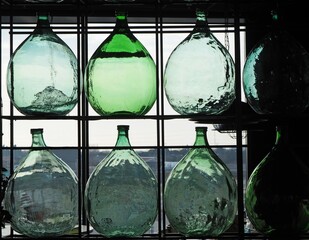 Large glass demijohns for wine against the light of a window