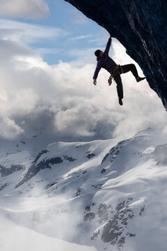 Adult adventurous man Rock Climbing a steep rocky cliff. Extreme adventure composite. 3d rendering mountain artwork. Aerial background landscape from British Columbia, Canada. Cloudy Sky