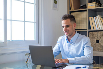 Portrait of handsome businessman typing on laptop keyboard at office. Happy caucasian male executive doing online work at home. Focused man entrepreneur at work typing on key pad with document and pen