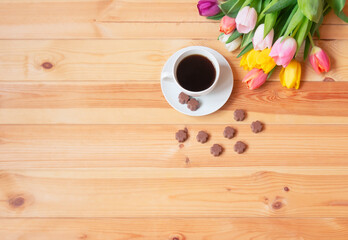 Cup of coffee, chocolate candies and colorful fresh spring tulips on wooden table.
