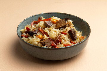 Traditional pilaf with beef in a plate on a brown background.