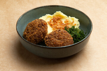 Meat cutlets and mashed potatoes in a plate on a brown background.