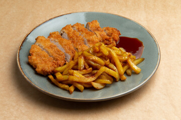 Fried chicken breast and fried potatoes in a plate on a brown background.
