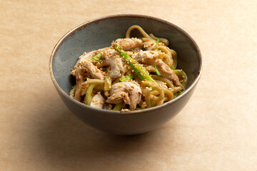 Wok with chicken and greens in a plate on a brown background.