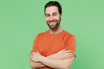 Young smiling happy cheerful positive confident caucasian man 20s wearing basic casual orange t-shirt hold hands crossed folded isolated on plain pastel light green color background studio portrait