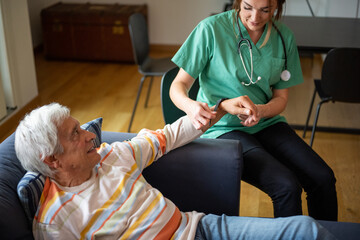 happy female nurse with a stethoscope visiting an elderly man, domestic medical assistant concept, female doctor of the medical health system putting a smartwatch on a old man