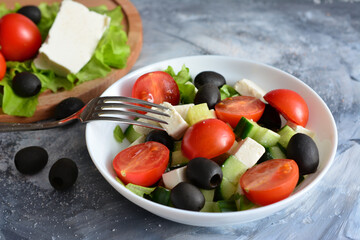 greek salad with black olives, tomatoes, cucumbers, feta cheese in white bowl with fork, close-up