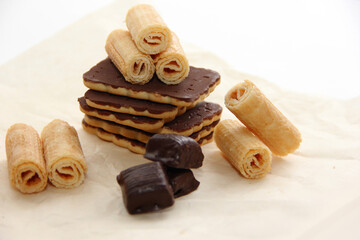 chocolate-covered cookies, waffle tubes and chocolates on parchment paper on a light background