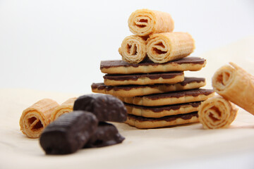 chocolate-covered cookies, waffle tubes and chocolates on parchment paper on a light background