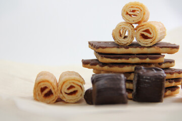 chocolate-covered cookies, waffle tubes and chocolates on parchment paper on a light background