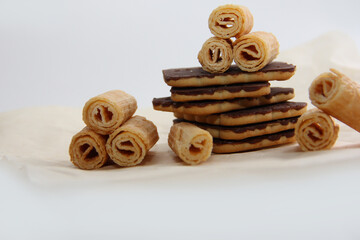 chocolate-covered cookies, waffle tubes and chocolates on parchment paper on a light background