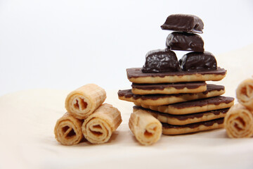 chocolate-covered cookies, waffle tubes and chocolates on parchment paper on a light background