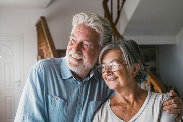 Senior couple relaxing looking out through window on a bright sunny day at home. Happy old husband and wife looking away and admiring view from modern house. Smiling elderly couple at home