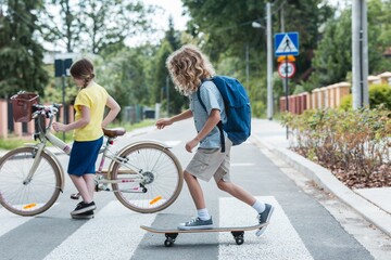 Boy on a skateboard and a girl with a bicycle cross the street - 490935920