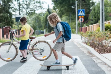 Tuinposter Boy on a skateboard and a girl with a bicycle cross the street © Photographee.eu