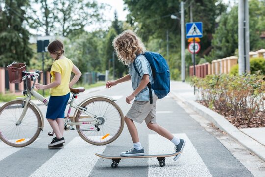 Boy on a skateboard and a girl with a bicycle cross the street