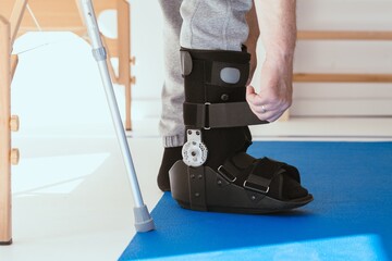 Injured patient in a leg brace exercising on a blue mat in a physiotherapy office