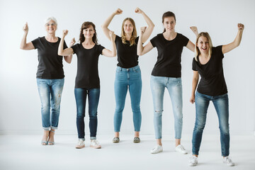Five women dressed in jeans and black T-shirts raise their hands in a gesture of strength