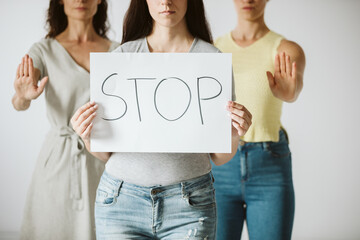Three young women are standing next to each other, one of them holding a piece of paper with the word stop