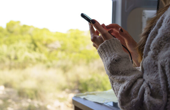 Horizontal image of a woman using her smart phone inside a camper van, with the door open to enjoy a beautiful day.