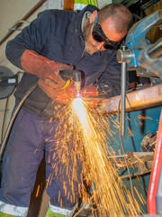 Professional welder using a plasma cutting machine with goggles and gloves.