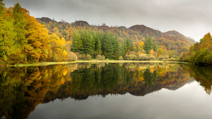 Fototapeta na wymiar Autumn Reflections at Yew Tree Tarn in the English Lake District National Park - One of the most accessible tarns – the road from Ambleside to Coniston goes right past it, with a small car park beside