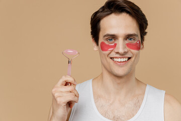 Young fun man 20s perfect skin wear pink patch under eye do face massage jade facial roller quartz...