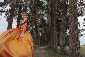 A young woman in an old orange dress walks on the shore of the lake near the castle