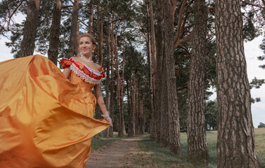 A young woman in an old orange dress walks on the shore of the lake near the castle