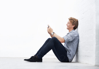 Sending an sms. A young man sitting in the studio and using his cellphone.