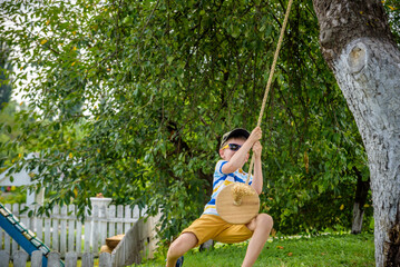 Happy little boy is having fun on a rope swing which he has found while having rest outside city. Active leisure time with children
