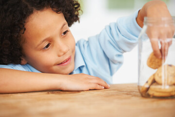 Mmm, so many cookies just for me. A cute young boy grabbing a cookie from the cookie jar.