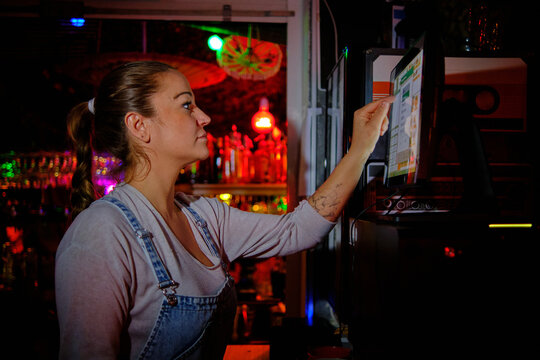 Female bartender using touch screen computer to register an order while working in a bar.