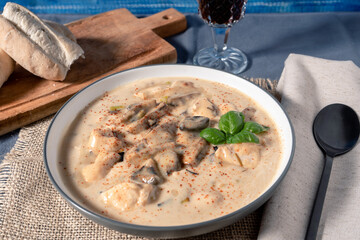 Homemade cream of chicken and mushroom soup or French style chicken fricassee with bread on a side, in a soup bowl on a wooden table. High view.