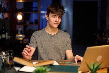 Teenage student learning at home with books and laptop computer. Online school and education,...