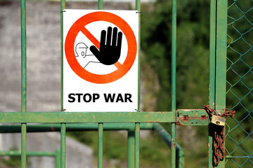 Red sign with large black hand indicating to stop and great message Stop War in english language on a Gate closed with padlock.