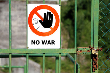 Gate closed with padlock and red sign with large black hand indicating to stop and great message NO WAR.