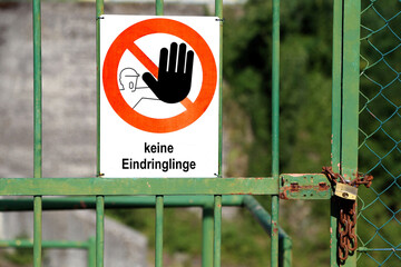 Red sign with large black hand indicating to stop and great message No Invaders in German language (keine eindringlinge) on a Gate closed with padlock
