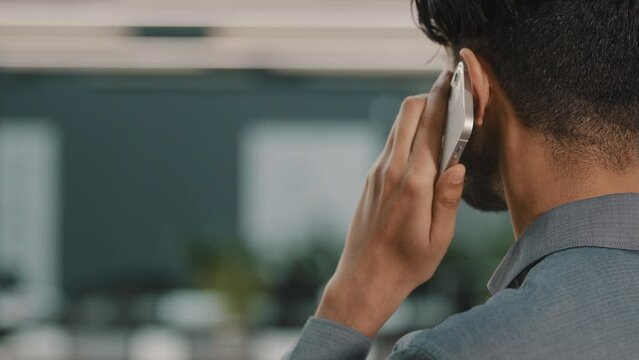 Back view of successful Arabian Indian businessman investor salesman making call talking in office enjoying mobile conversation indoors communicate with partner close up of male speaking cell phone