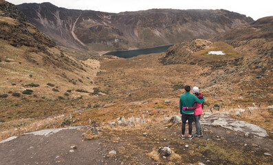 Adventurous couple hug and gaze at a breathtaking glacier valley landscape with a lake