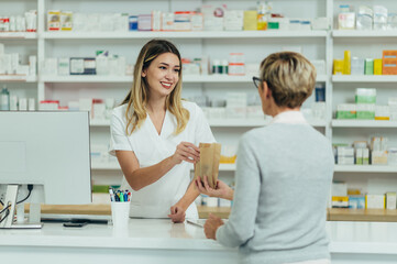 Female pharmacist selling medications at drugstore to a senior woman customer - obrazy, fototapety, plakaty