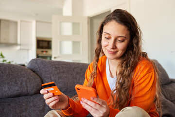 Woman dressed in orange colors shopping with her smartphone from the sofa