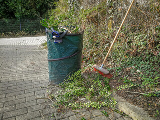 Garden Maintenance work. Green gardener bag and broom. Spring Hedge trimming at fence on a property boundary