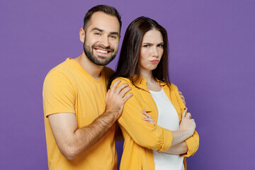 Young smiling displeased sad couple two friends family man woman together in yellow casual clothes try to hug offended girlfriend after argument isolated on plain violet background studio portrait.