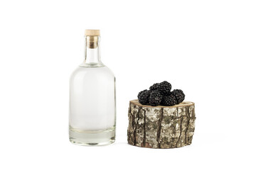 Transparent glass bottle with alcohol liquid and ripe blackberry on white background. Creative...