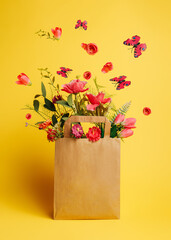 Paper bag with fresh flowers and butterflies flying against vibrant yellow background. Creative...