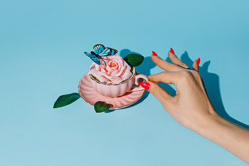 Creative layout with woman's hand holding teapot with fresh rose flower and butterfly on pastel...