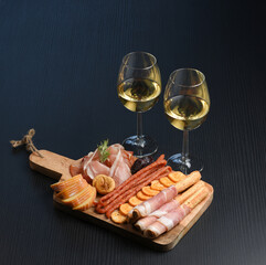 Two white wine glasses with buffet platter with cheese and meats, antipasti, prosciutto, charcuterie. Delicatessen appetizer